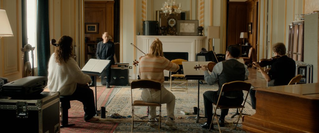 Les quatre musicien·nes du film de Grégory Magne répètent, de dos, dans un appartement parisien. Face à eux, un homme en costume sombre les dirige.